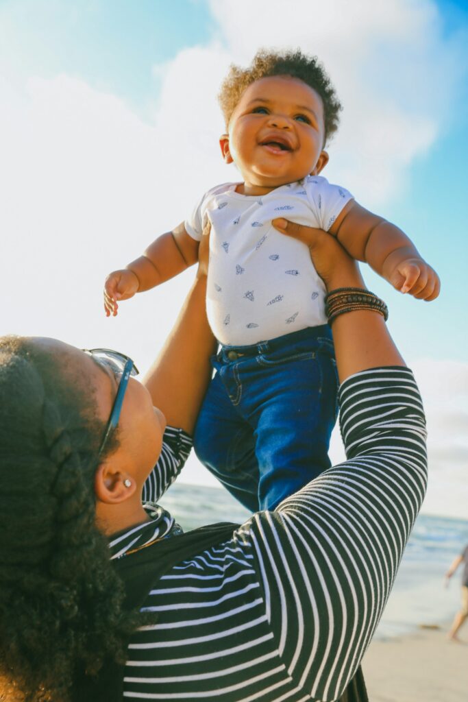 Smiling baby being lifted into the air by a parent at the beach