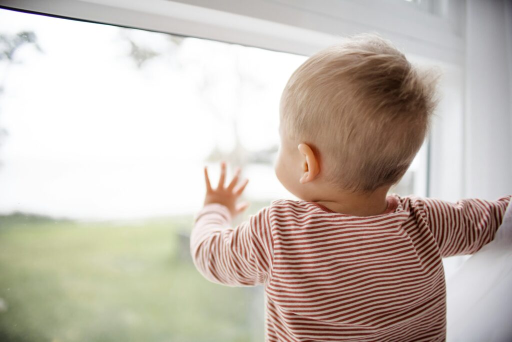 Toddler in a striped shirt looking out of a window