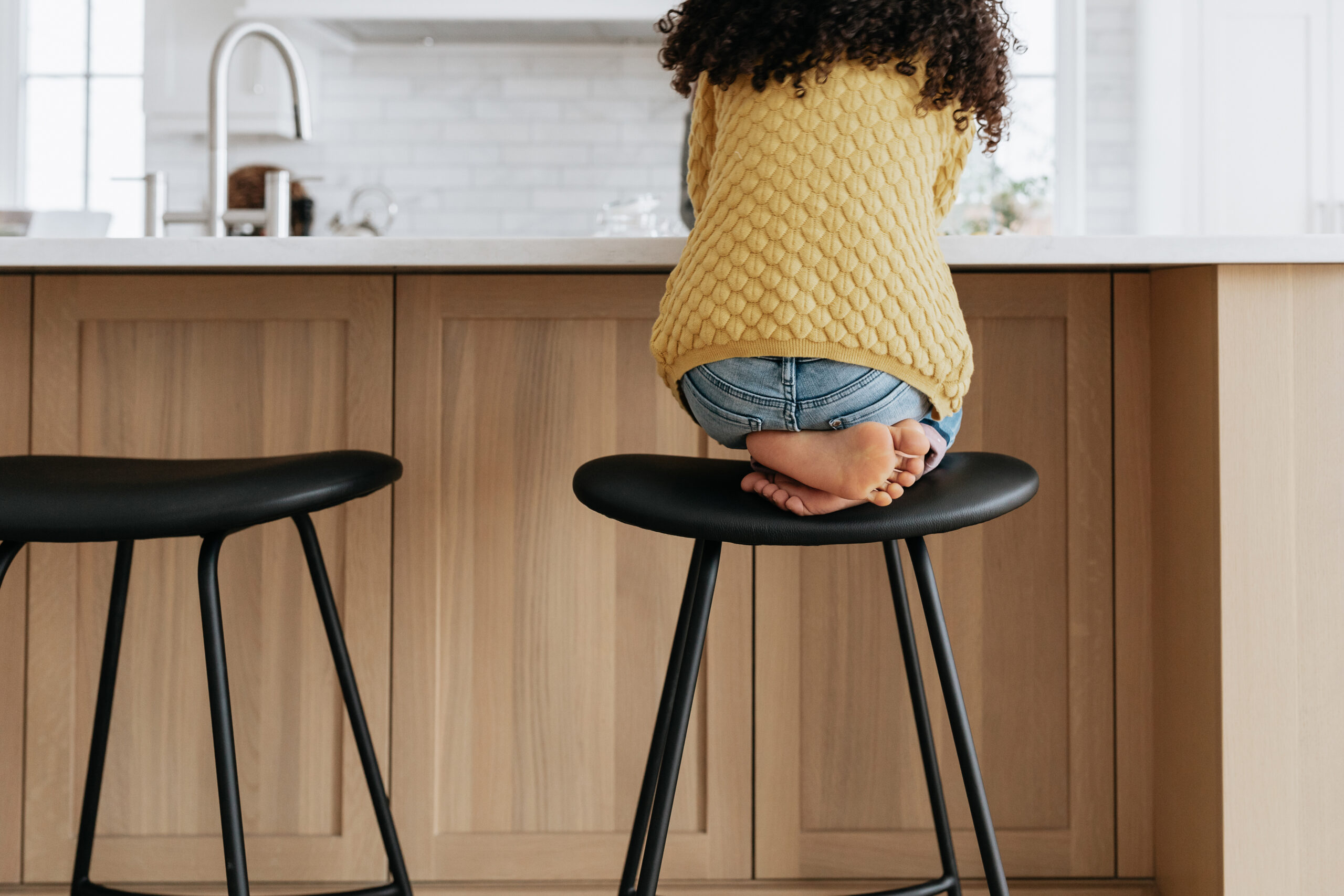 Child sitting cross-legged on a stool at the kitchen counter