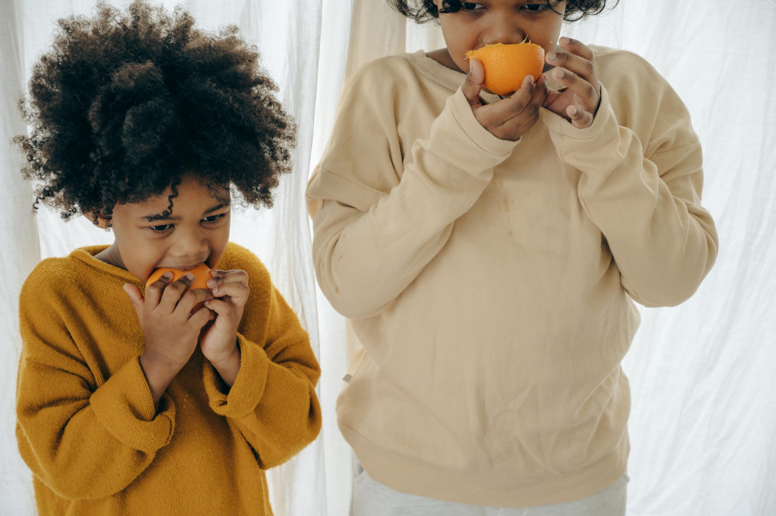 Two kids eating oranges