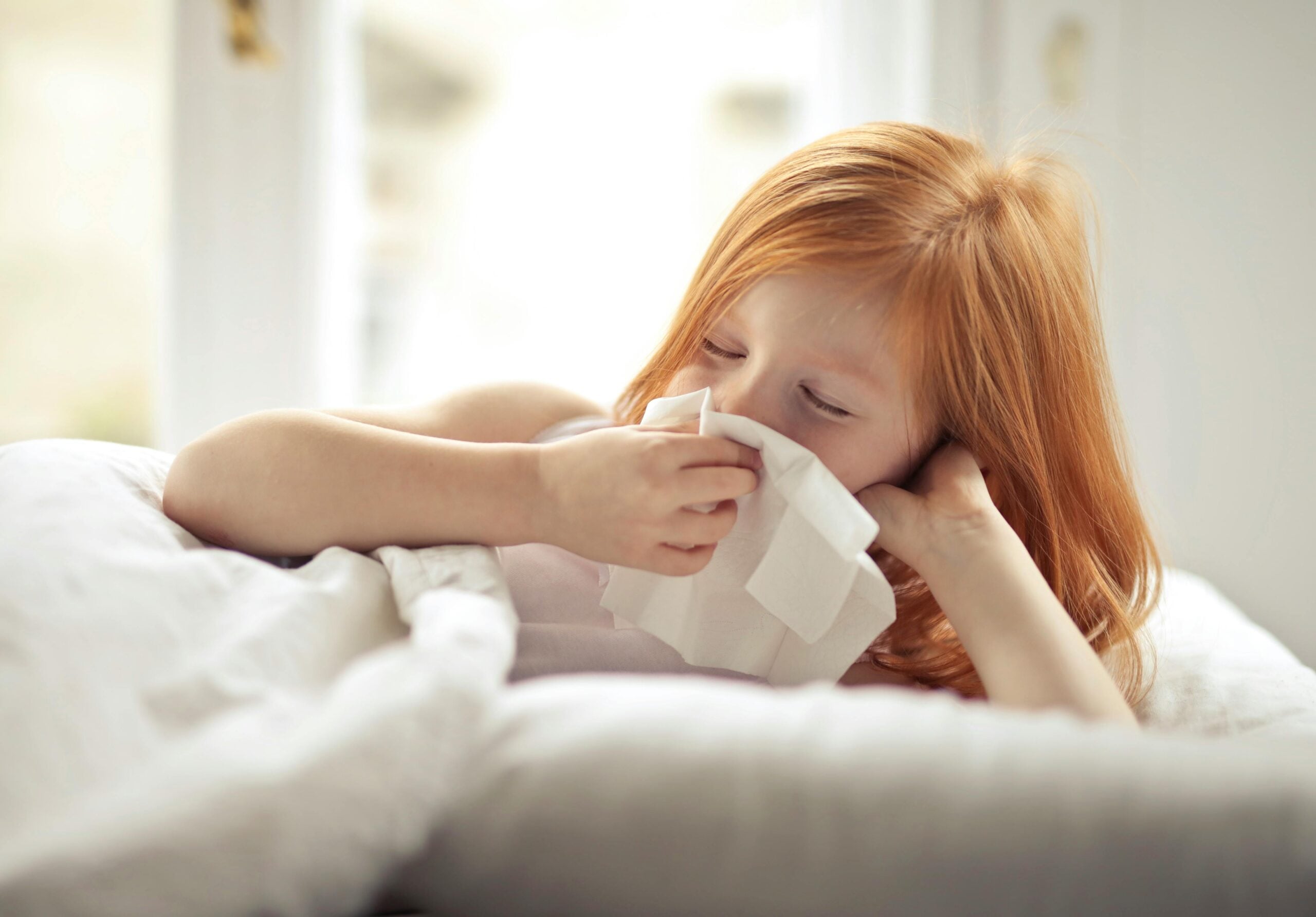 Sick child blowing her nose with a tissue