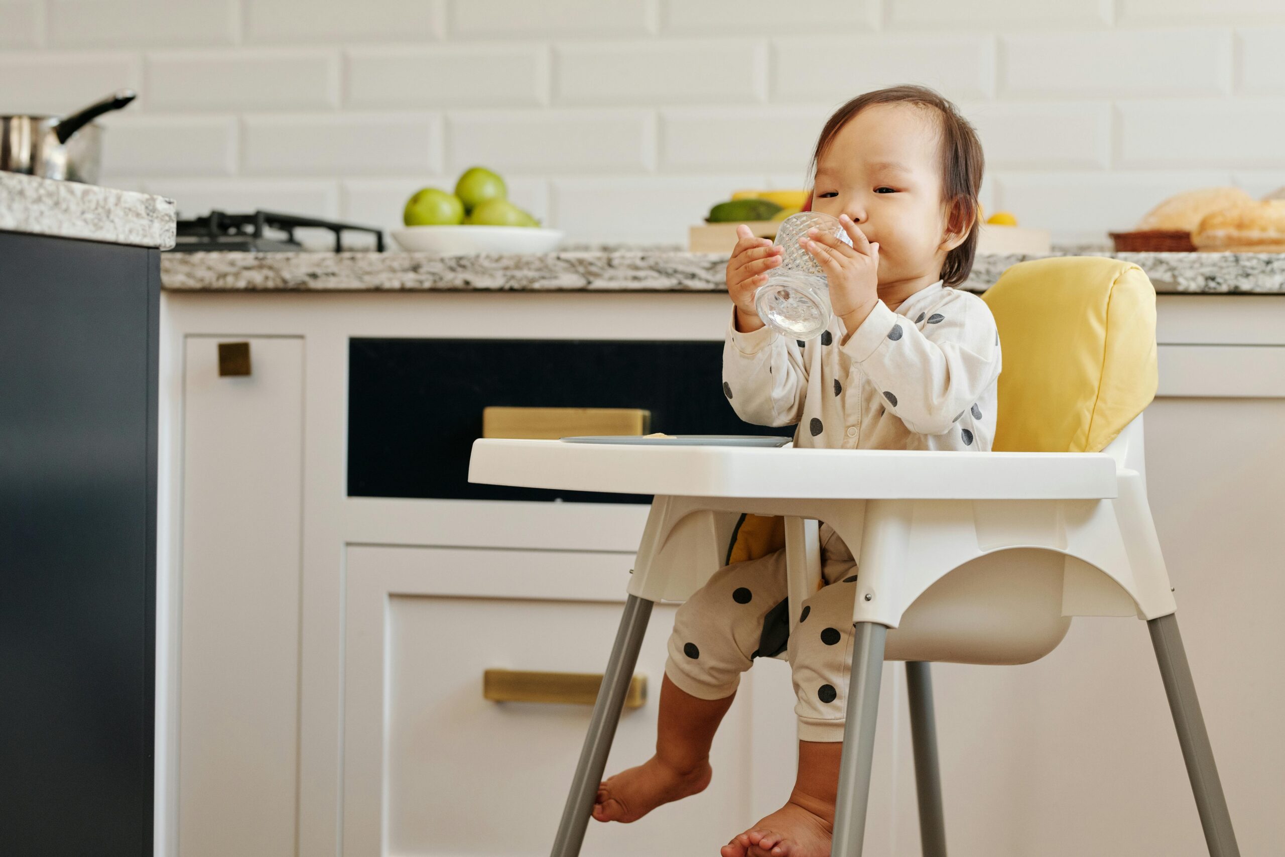 Infant in high chair drinking water from a glass