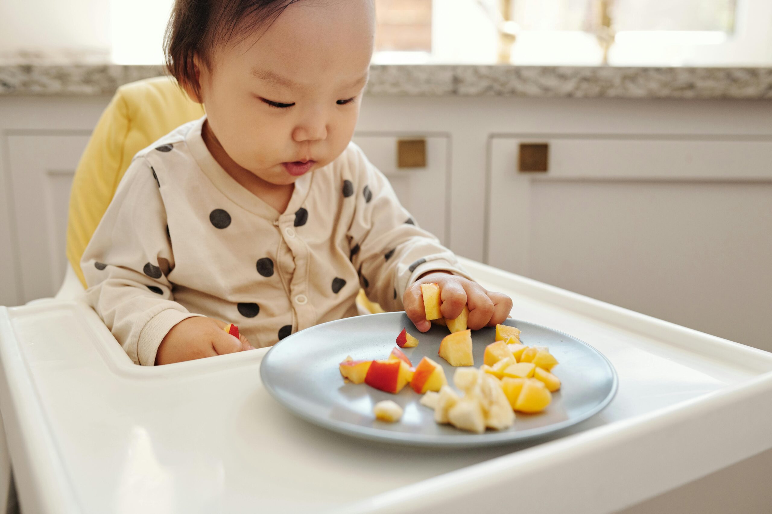 Infant in a high chair eating pieces of fruit